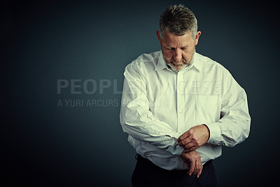 Buy stock photo Studio shot of a handsome mature businessman buttoning his sleeves while sitting down against a dark background