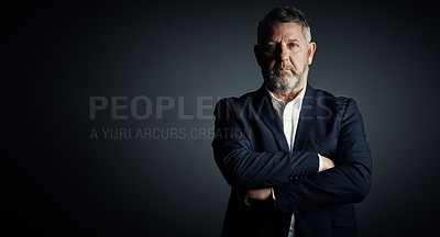 Buy stock photo Studio portrait of a handsome mature businessman standing with his arms folded against a dark background