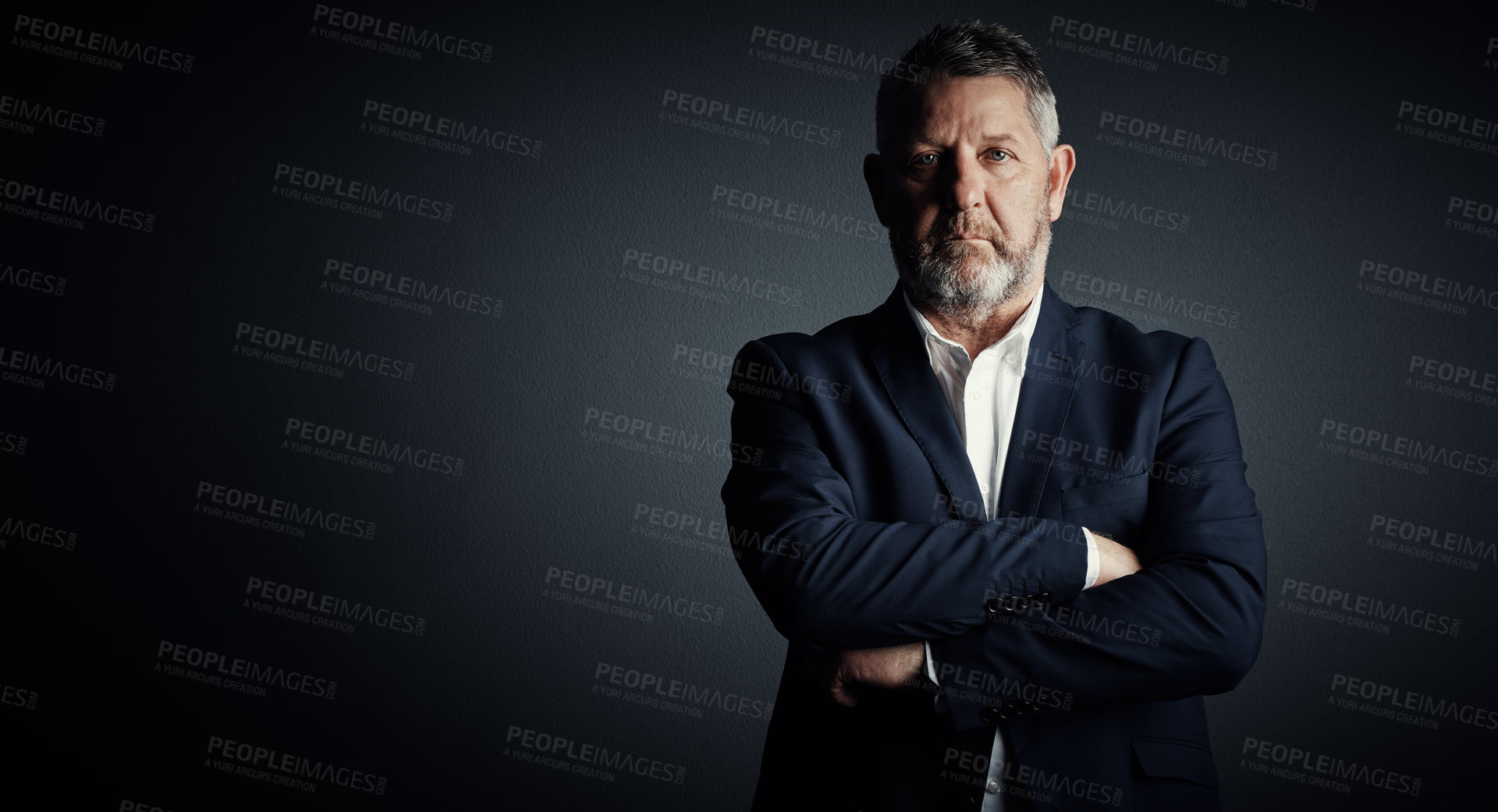 Buy stock photo Studio portrait of a handsome mature businessman standing with his arms folded against a dark background