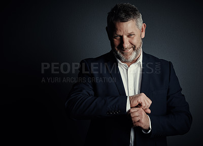 Buy stock photo Studio portrait of a handsome mature businessman buttoning his sleeves while standing against a dark background