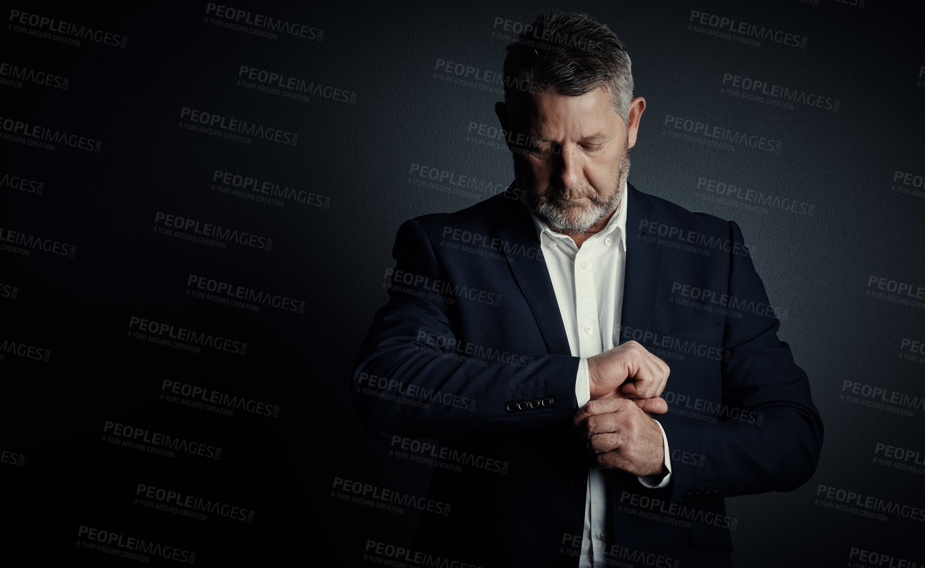 Buy stock photo Studio shot of a handsome mature businessman buttoning his sleeves while standing against a dark background