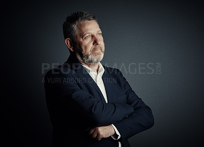 Buy stock photo Studio shot of a handsome mature businessman looking thoughtful while standing with his arms folded against a dark background