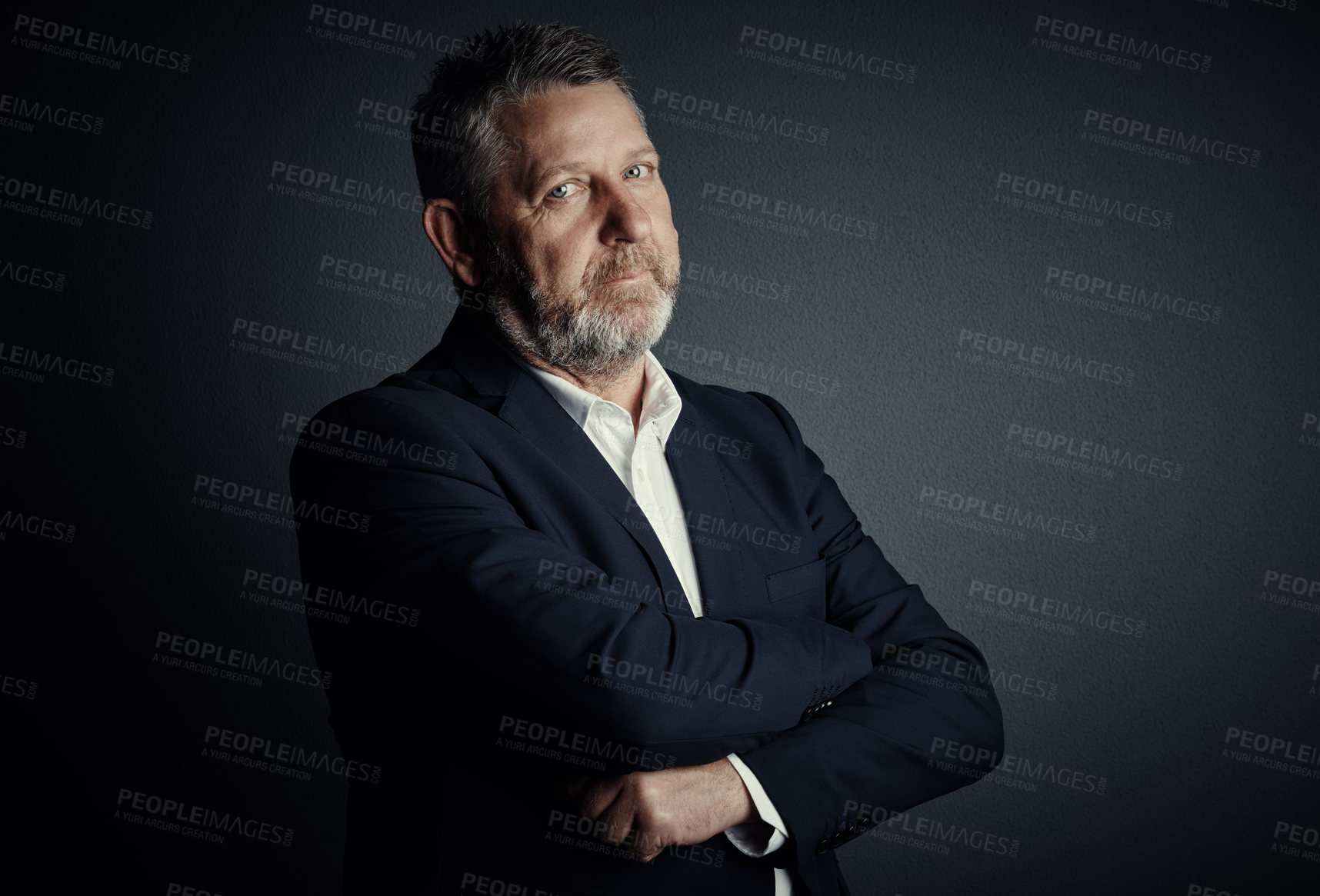 Buy stock photo Studio portrait of a handsome mature businessman standing with his arms folded against a dark background