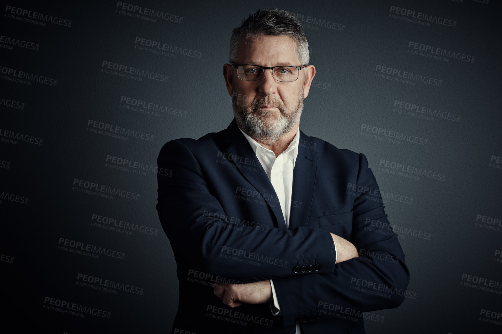 Buy stock photo Studio portrait of a handsome mature businessman standing with his arms folded against a dark background