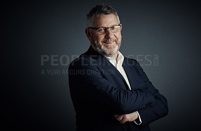 Buy stock photo Studio portrait of a handsome mature businessman standing with his arms folded against a dark background