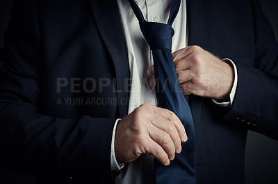 Buy stock photo Studio shot of an unrecognizable mature businessman fastening his tie while standing against a dark background