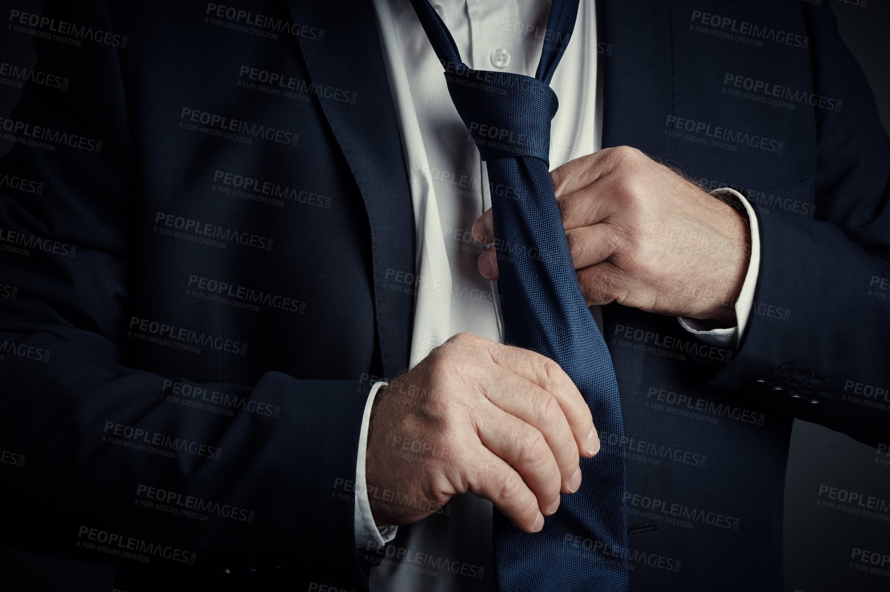 Buy stock photo Studio shot of an unrecognizable mature businessman fastening his tie while standing against a dark background