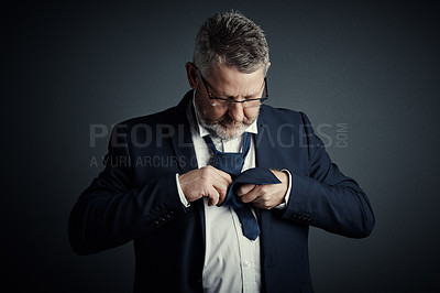Buy stock photo Studio shot of a handsome mature businessman fastening his tie while standing against a dark background