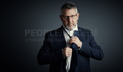 Buy stock photo Studio portrait of a handsome mature businessman fastening his tie while standing against a dark background