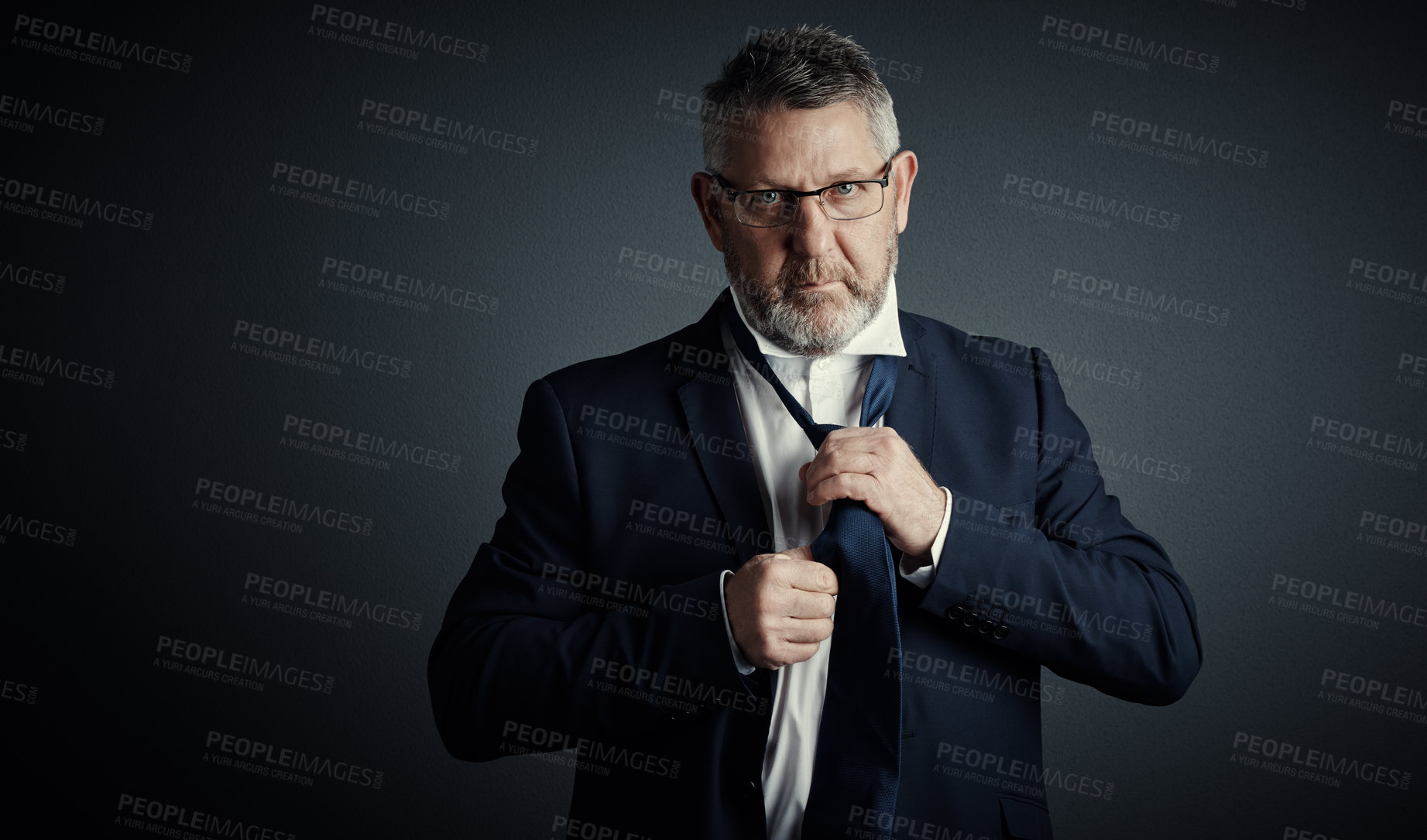 Buy stock photo Studio portrait of a handsome mature businessman fastening his tie while standing against a dark background