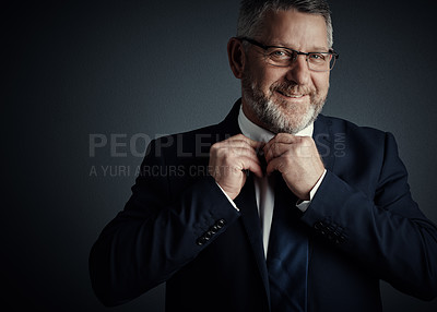Buy stock photo Studio portrait of a handsome mature businessman fastening his tie while standing against a dark background