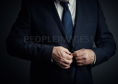 Buy stock photo Studio shot of an unrecognizable mature businessman buttoning his jacket while standing against a dark background
