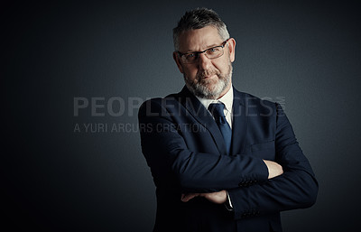 Buy stock photo Studio portrait of a handsome mature businessman standing with his arms folded against a dark background