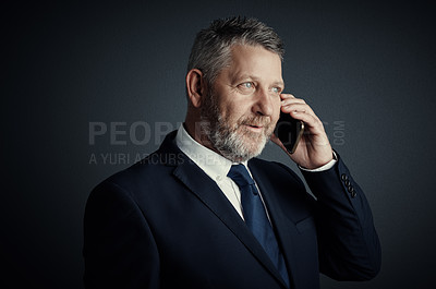 Buy stock photo Studio shot of a handsome mature businessman looking thoughtful while making a call against a dark background