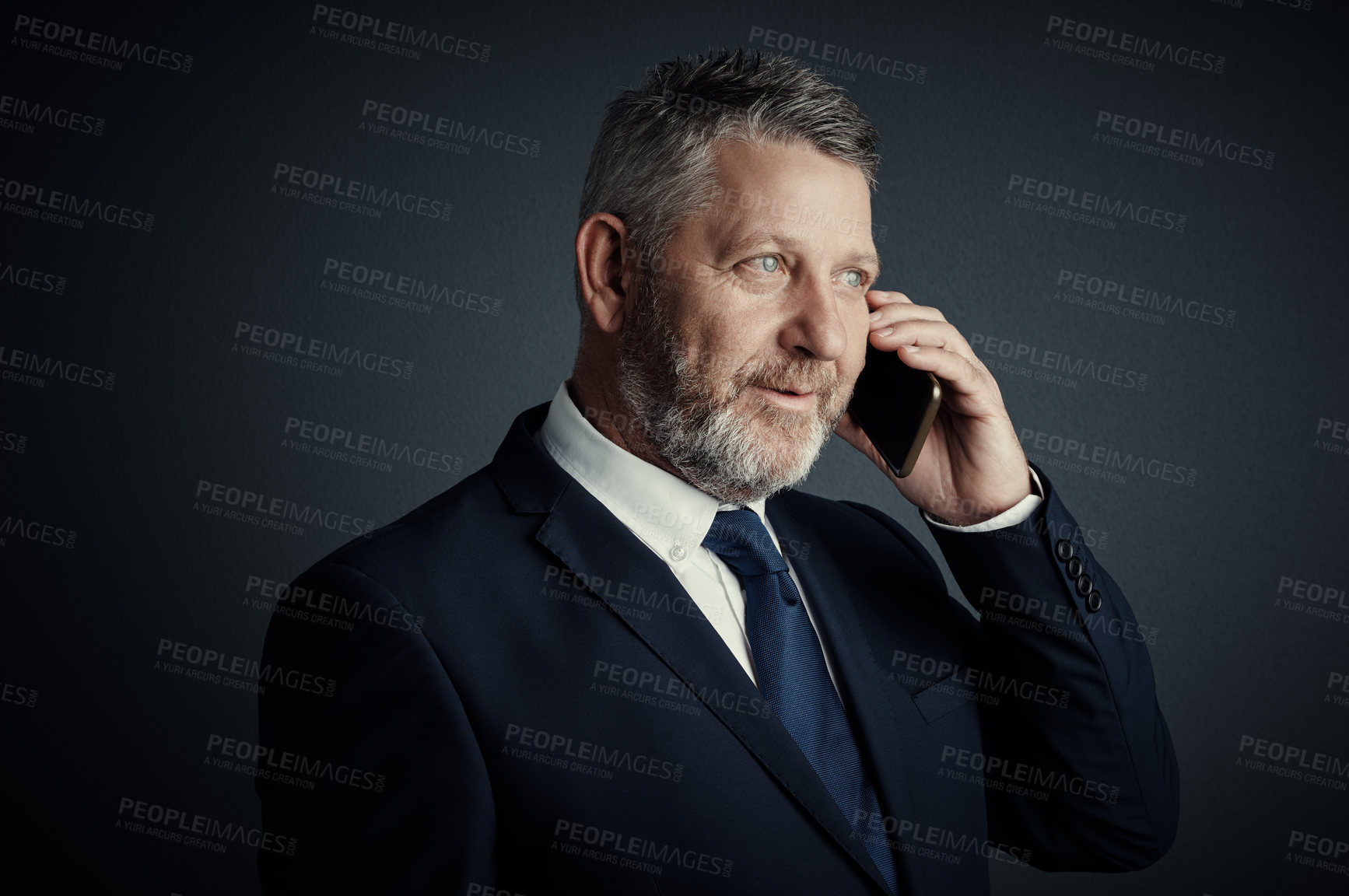 Buy stock photo Studio shot of a handsome mature businessman looking thoughtful while making a call against a dark background