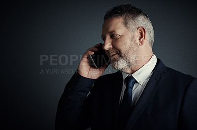 Buy stock photo Studio shot of a handsome mature businessman looking thoughtful while making a call against a dark background