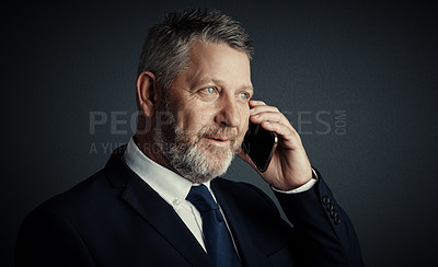 Buy stock photo Studio shot of a handsome mature businessman looking thoughtful while making a call against a dark background