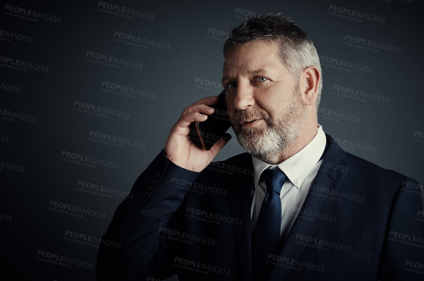 Buy stock photo Studio shot of a handsome mature businessman looking thoughtful while making a call against a dark background