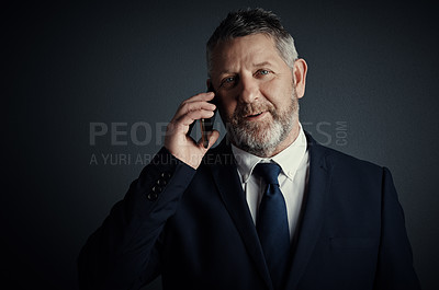 Buy stock photo Studio portrait of a handsome mature businessman looking thoughtful while making a call against a dark background