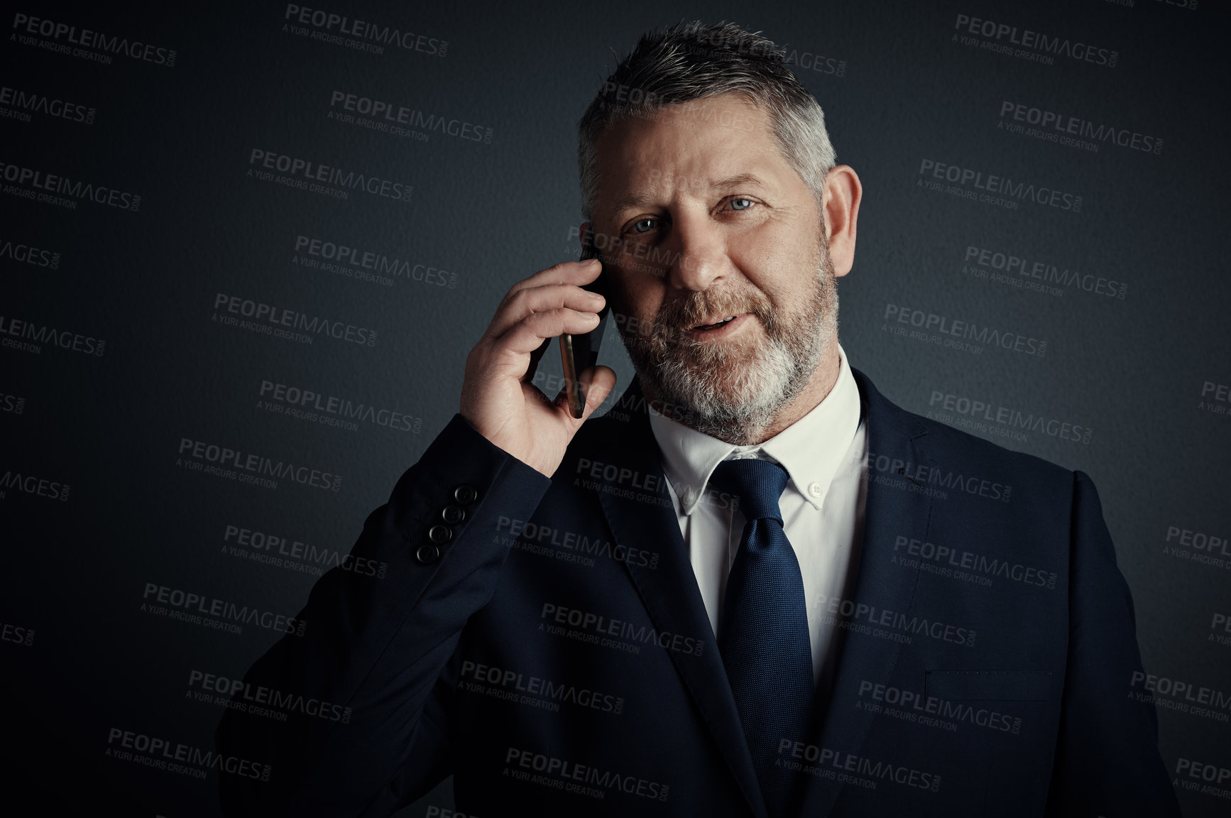 Buy stock photo Studio portrait of a handsome mature businessman looking thoughtful while making a call against a dark background