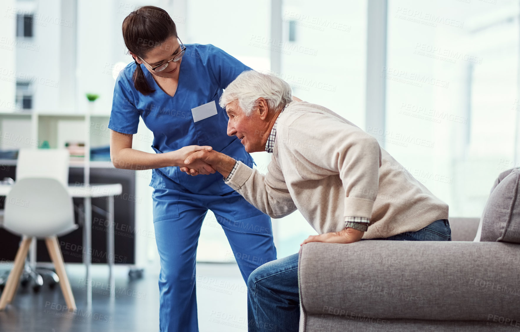 Buy stock photo Cropped shot of a young female nurse helping her senior patient up from a chair in the old age home