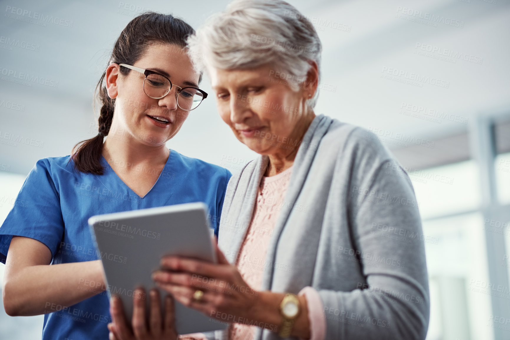 Buy stock photo Cropped shot of a young female nurse and her senior patient looking at a tablet in the old age home