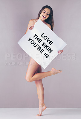 Buy stock photo Studio shot of an attractive young woman holding a sign that reads “love the skin you're in” against a pink background