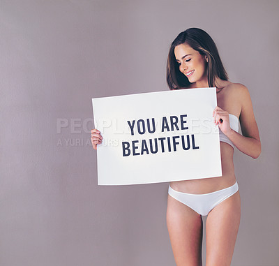 Buy stock photo Studio shot of an attractive young woman holding a sign that reads “you are beautiful” against a pink background