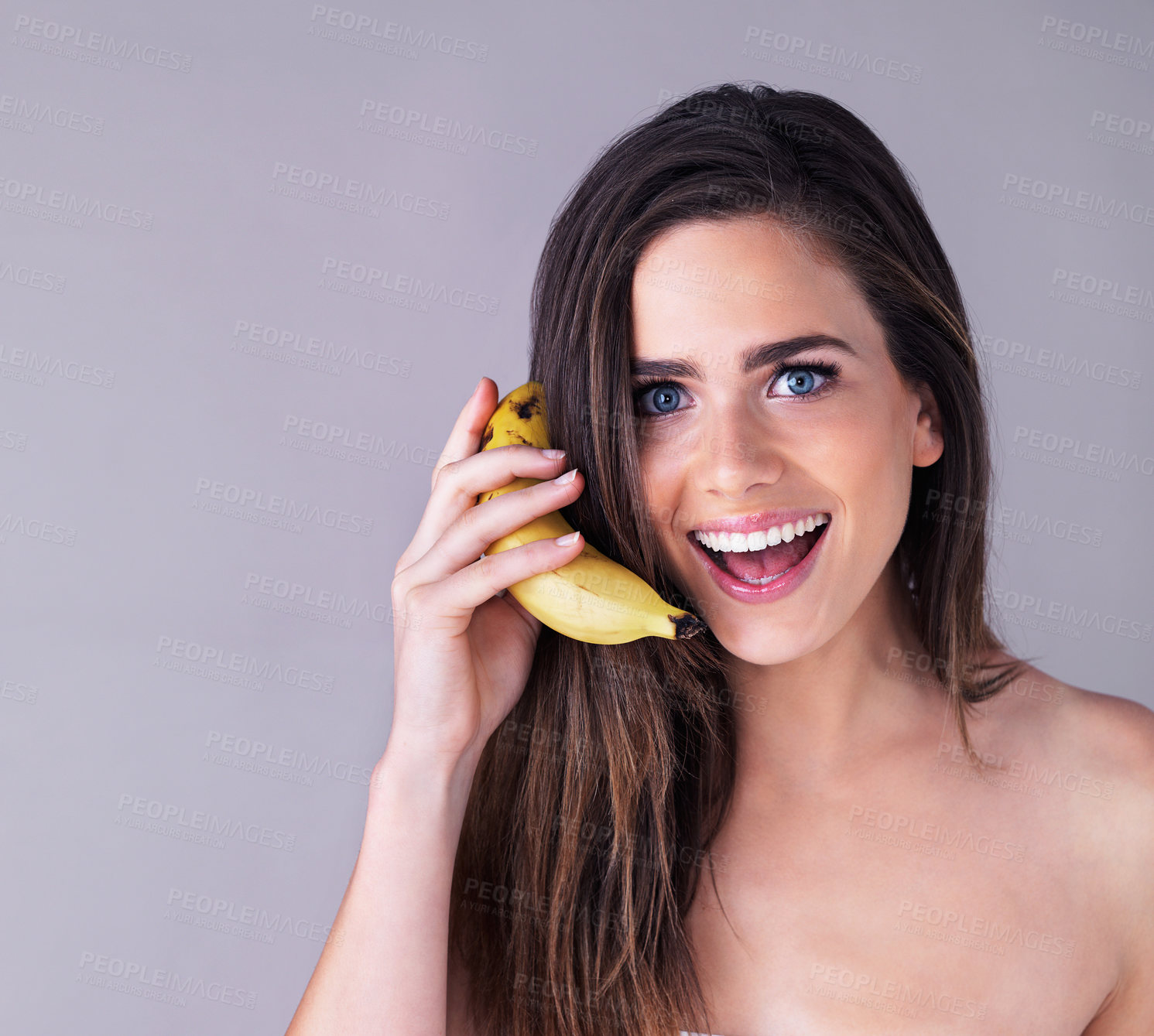 Buy stock photo Studio portrait of an attractive young woman pretending to use a banana as a phone against a purple background