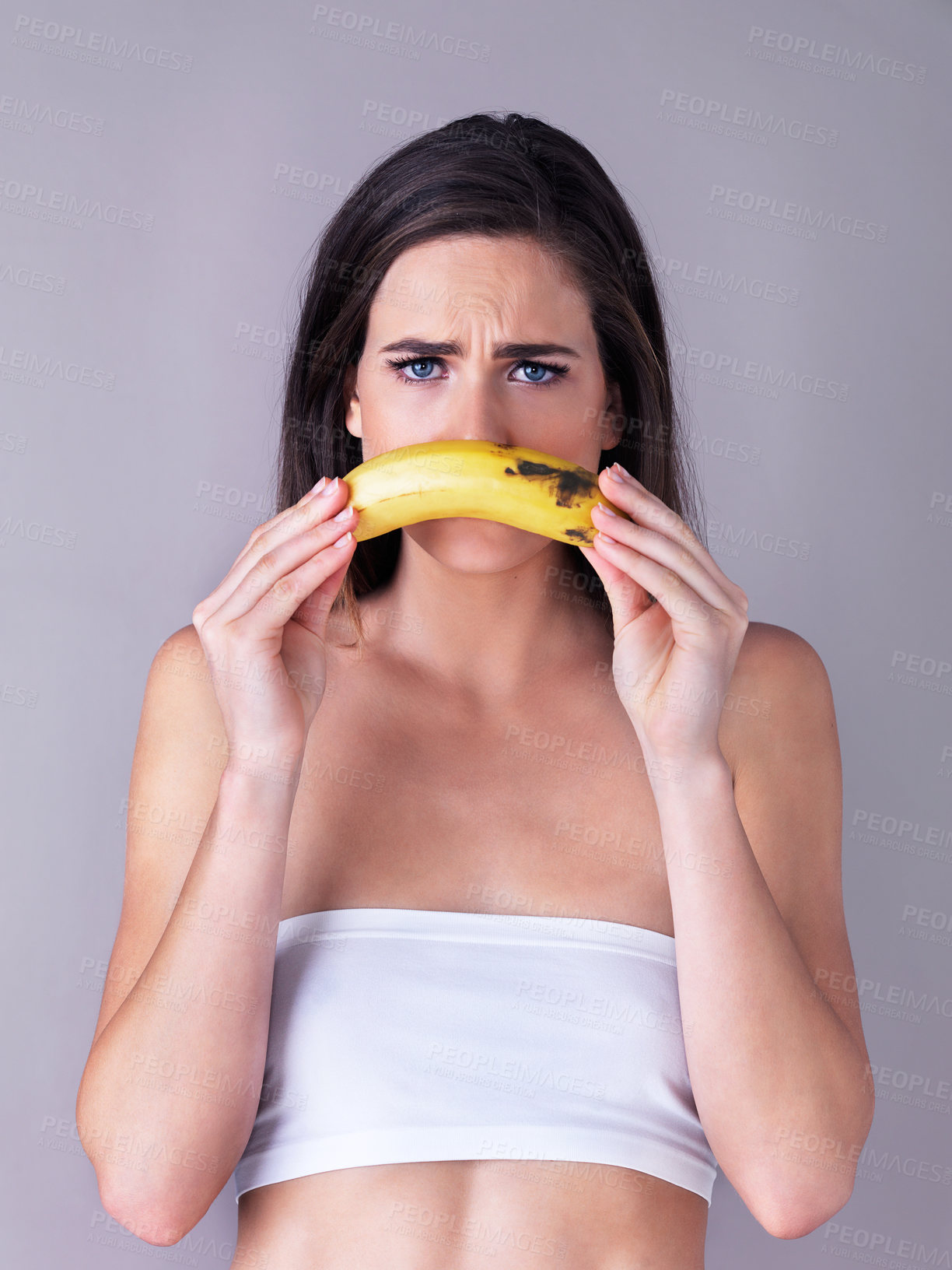 Buy stock photo Studio portrait of an attractive young woman holding a banana against a purple background