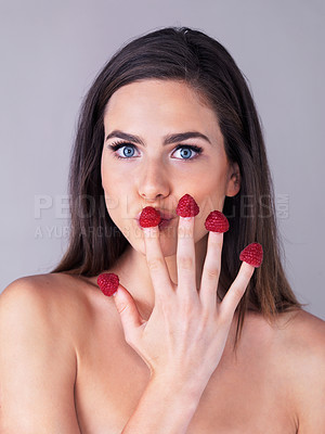 Buy stock photo Studio portrait of an attractive young woman eating raspberries off her fingertips against a purple background