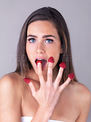 Buy stock photo Studio portrait of an attractive young woman eating raspberries off her fingertips against a purple background