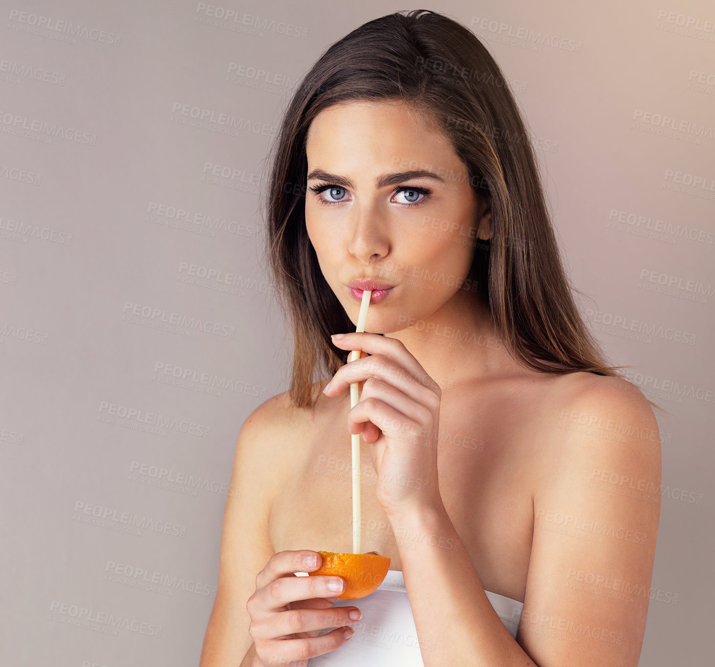 Buy stock photo Studio portrait of an attractive young woman drinking from an orange against a purple background