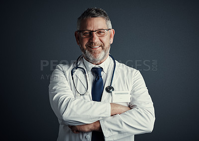 Buy stock photo Studio portrait of a handsome mature male doctor standing with his arms folded against a dark background