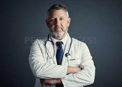 Buy stock photo Studio portrait of a handsome mature male doctor standing with his arms folded against a dark background