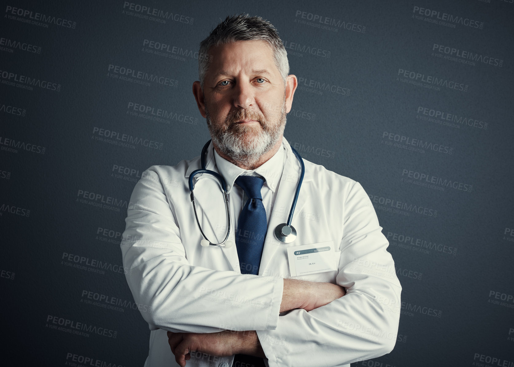 Buy stock photo Studio portrait of a handsome mature male doctor standing with his arms folded against a dark background