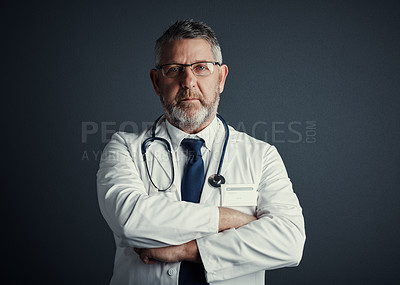 Buy stock photo Studio portrait of a handsome mature male doctor standing with his arms folded against a dark background