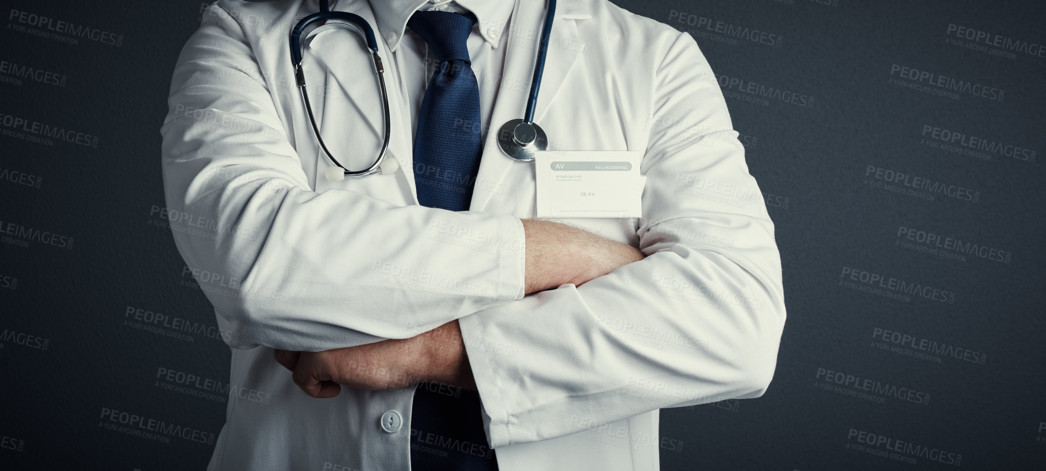 Buy stock photo Studio shot of an unrecognizable male doctor standing with his arms folded against a dark background