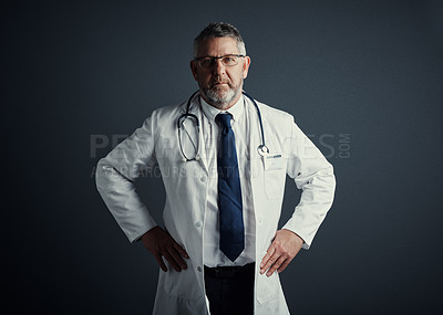 Buy stock photo Studio portrait of a handsome mature male doctor standing with his hands on his hips against a dark background