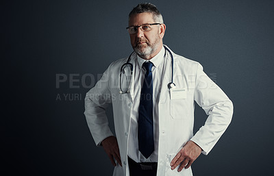 Buy stock photo Studio portrait of a handsome mature male doctor standing with his hands on his hips against a dark background