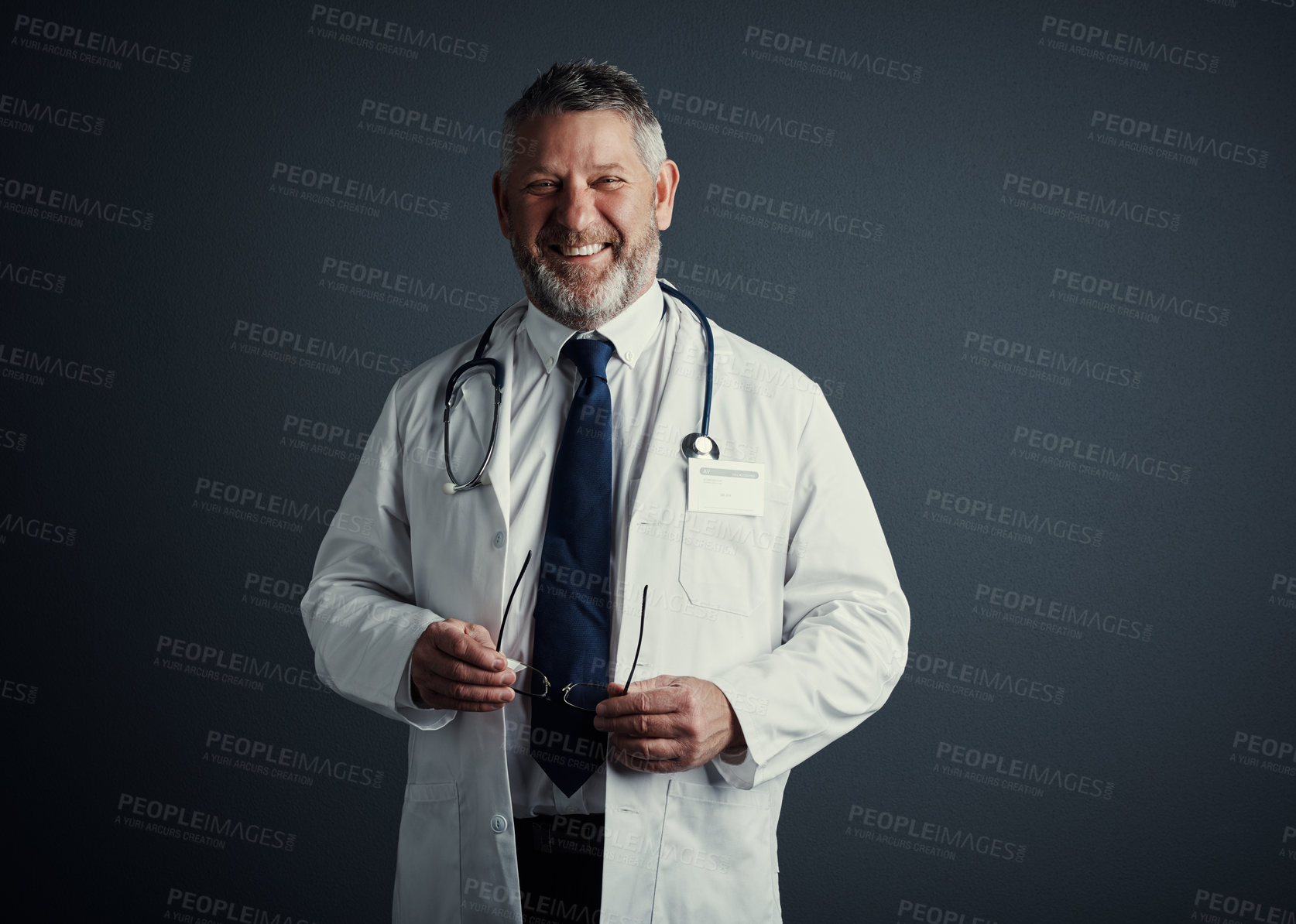 Buy stock photo Studio portrait of a handsome mature male doctor standing against a dark background