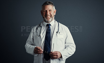 Buy stock photo Studio shot of a handsome mature male doctor looking thoughtful while standing against a dark background