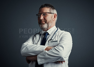 Buy stock photo Studio shot of a handsome mature male doctor looking thoughtful while standing with his arms folded against a dark background