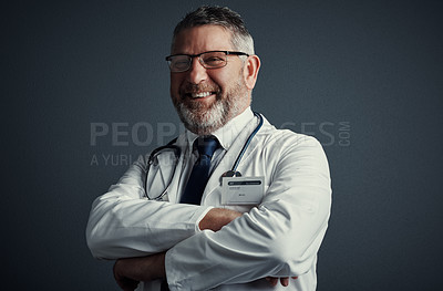 Buy stock photo Studio portrait of a handsome mature male doctor standing with his arms folded against a dark background