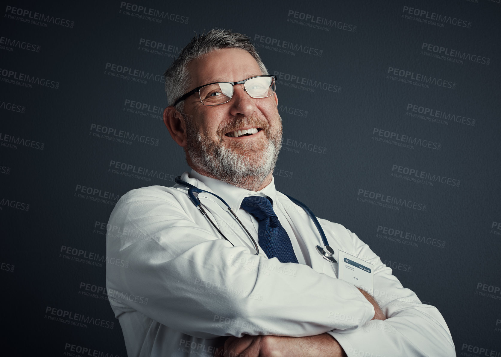 Buy stock photo Studio portrait of a handsome mature male doctor standing with his arms folded against a dark background