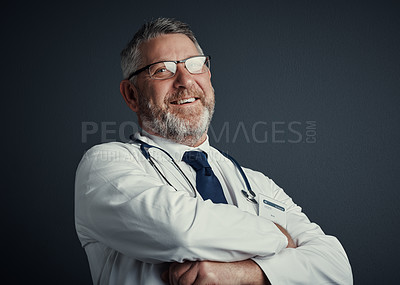 Buy stock photo Studio portrait of a handsome mature male doctor standing with his arms folded against a dark background