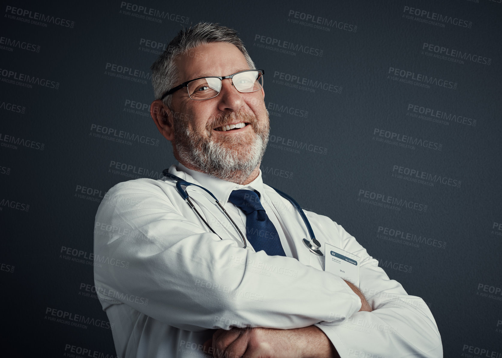 Buy stock photo Studio portrait of a handsome mature male doctor standing with his arms folded against a dark background