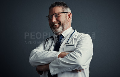 Buy stock photo Studio shot of a handsome mature male doctor looking thoughtful while standing with his arms folded against a dark background