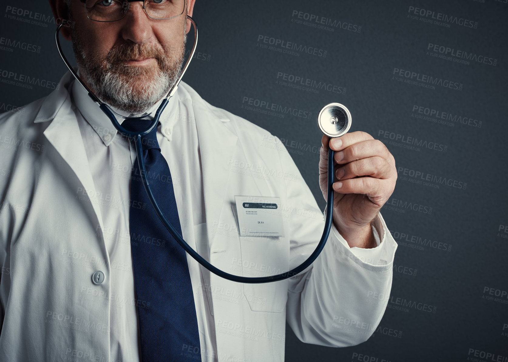 Buy stock photo Studio portrait of a handsome mature male doctor holding a stethoscope against a dark background