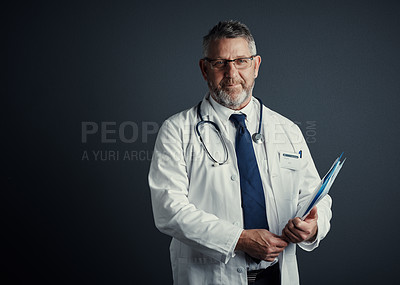 Buy stock photo Studio portrait of a handsome mature male doctor holding medical records while standing against a dark background